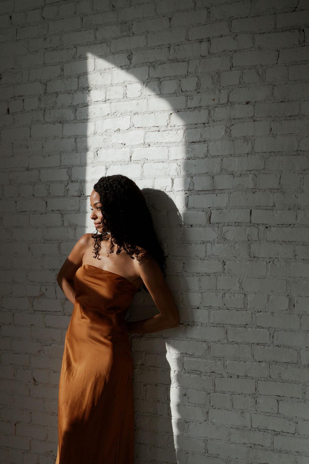 Charlie Smith leaning against a white brick wall in a shaft of sunlight